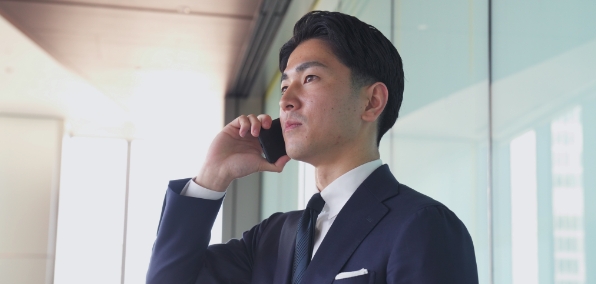 携帯電話を片手に通話をする男性のビジネスマンの写真